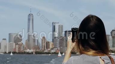 年轻美丽的旅游女孩在美国纽约曼哈顿的智能手机上从东河的船上拍照。